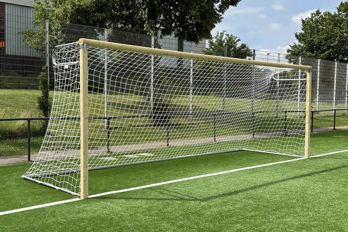 Fußballtor aus Holz mit Aluminiumverbindern, weißem Tornetz und Aluminiumbodenhülsen auf dem Kunstrasen eines Sportplatzes.